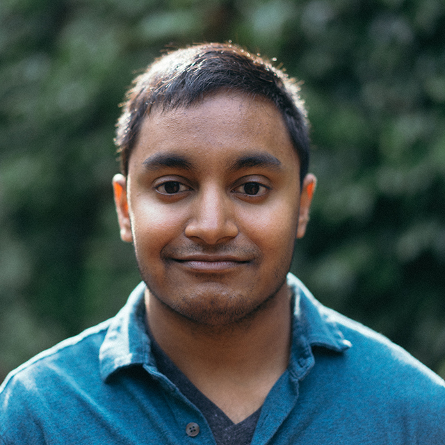 Headshot of Ary Maharaj. Ary is a cis man of Asian-Caribbean descent, with short straight black hair parted to the side. He is standing in front of a group of trees and is wearing a green, short-sleeved button up shirt.
