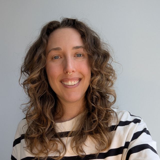 A headshot of Deidre, looking into the camera. She has long brown hair and is smiling.
