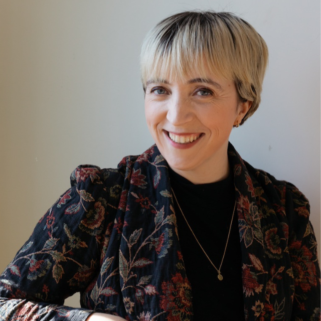 A portrait shot of Alice. She has dyed blond hair and is smiling, wearing a floral print shirt.